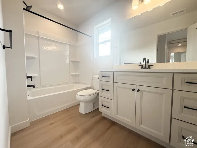 Bathroom featuring a white vanity with light-toned countertop, integrated basin, matte black hardware, wood-finish flooring, and a bathtub-shower combination with a surround