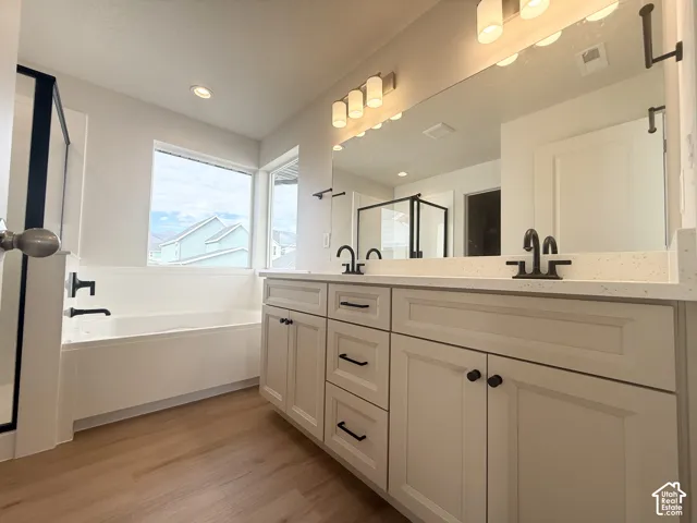 Double vanity featuring white shaker-style cabinetry, quartz countertops, matte black hardware, and wood-finish flooring, complemented by a deep soaking tub