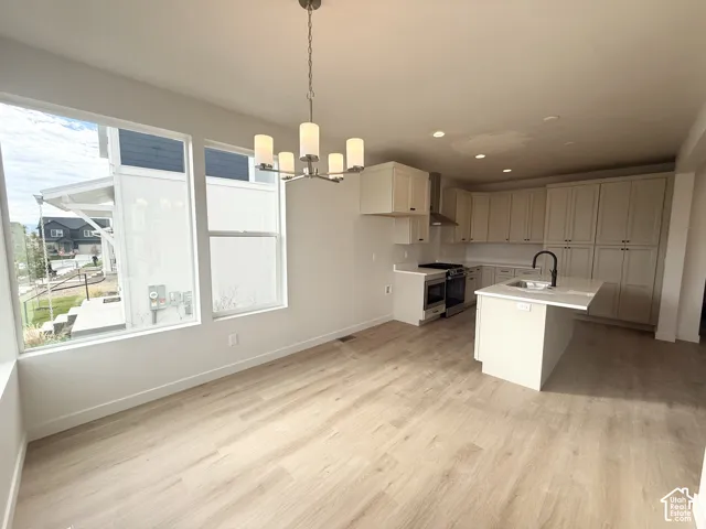 Open-concept kitchen featuring shaker-style cabinetry, a central island with a quartz countertop, stainless steel appliances, wood-finish flooring, and a multi-light chandelier