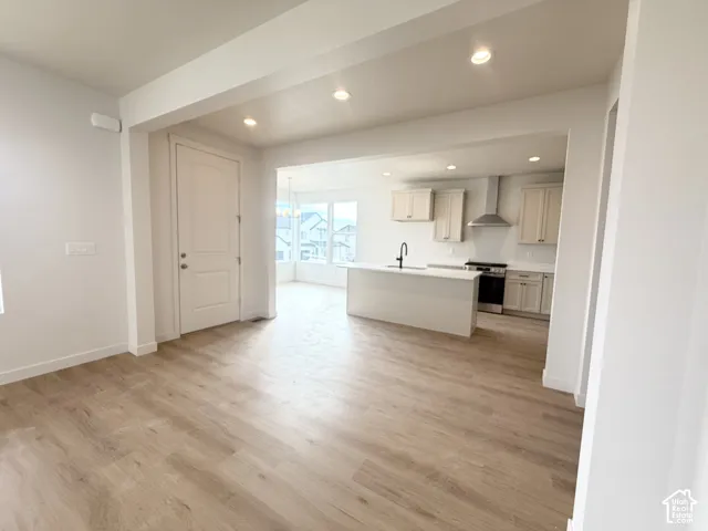 Wood-finish flooring, kitchen island with sink, stainless steel range hood, recessed lighting, and white shaker-style cabinetry