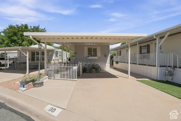 Covered carport with metal awning, concrete parking pad, and white picket fencing
