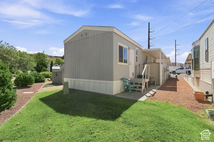 Exterior siding with neutral finish, attached covered patio, concrete landing, and low-maintenance landscaping featuring gravel ground cover and manicured lawn