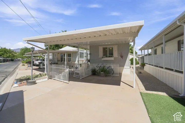 Covered carport with integrated concrete driveway, attached white metal picket fencing, and exterior window shutters