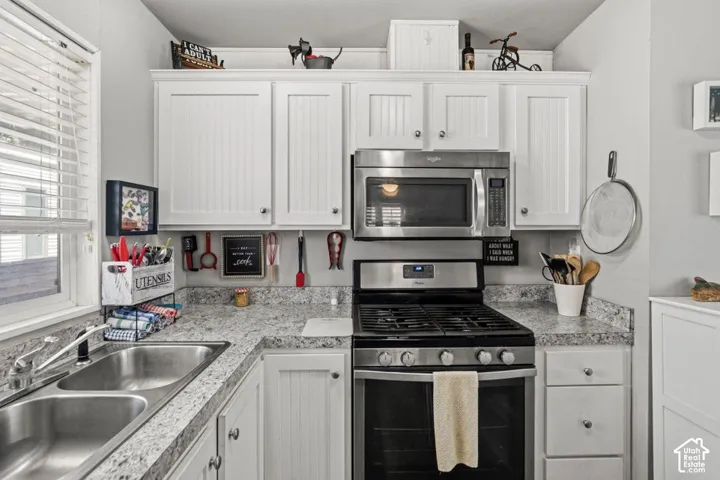 Kitchen featuring white beadboard cabinetry, stainless steel microwave, gas range, stone-patterned countertops, and a dual-basin stainless steel sink