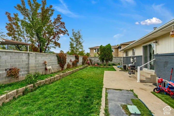 Fenced backyard featuring a concrete patio, retaining wall, lawn area, and mature trees