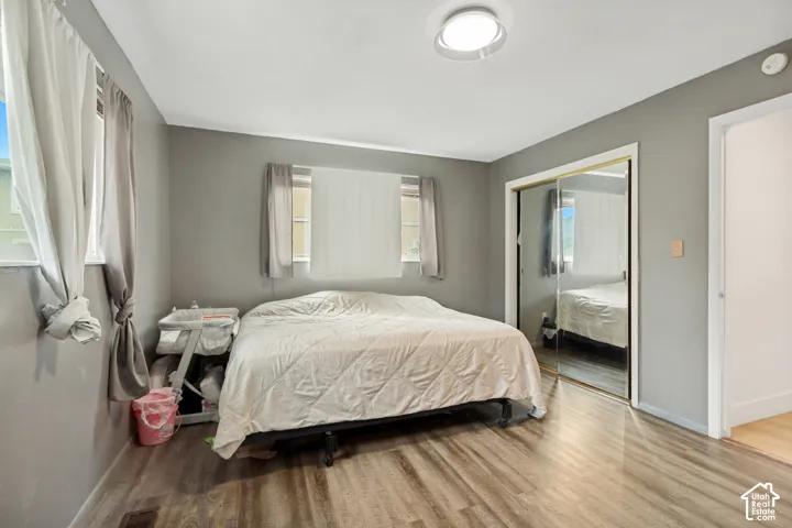 Bedroom interior featuring wood-finish flooring, neutral wall paint, dual-pane windows, and a sliding mirrored closet door with gold-tone framing