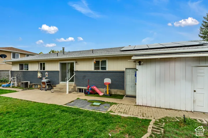 Exterior featuring a painted brick and siding facade, rooftop solar panel array, concrete patio, and attached storage structure