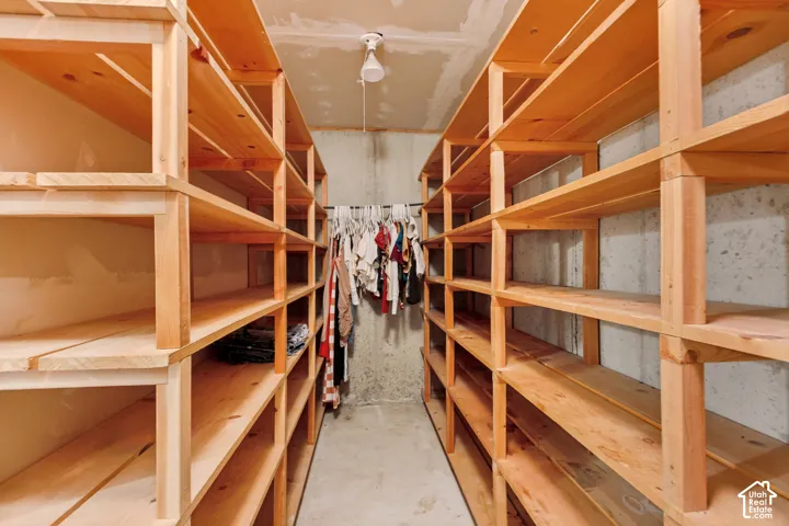 Storage area featuring floor-to-ceiling built-in wooden shelving units, concrete walls, and a hanging rod