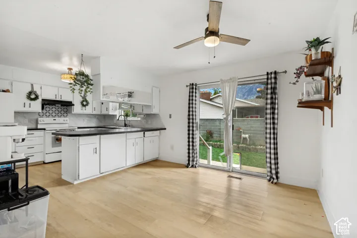 Kitchen featuring white cabinetry, dark countertops, patterned tile backsplash, wood-finish flooring, and sliding glass patio doors