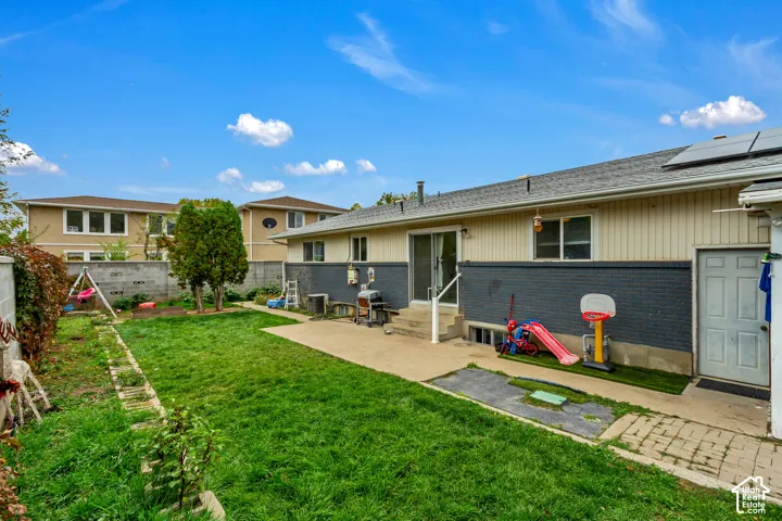 Exterior backyard featuring a concrete patio, brick and horizontal siding facade, concrete masonry block perimeter wall, and solar panels
