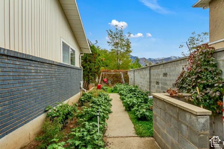 Exterior side yard featuring a concrete path, masonry perimeter wall, dark brick cladding, and mountain backdrop