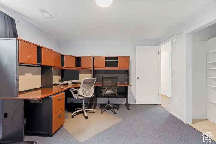 Built-in cherry-tone cabinetry featuring overhead storage and desk surface, neutral carpeting, and a recessed reach-in closet with integrated shelving