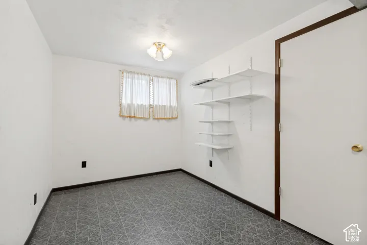 Interior space featuring dark patterned tile flooring, white walls, wall-mounted adjustable shelving, and a flush-mount light fixture