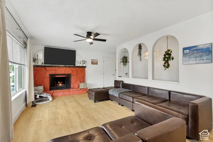 Living area featuring stone-clad fireplace, wood-finish flooring, three arched wall niches, and ceiling fan with integrated lighting