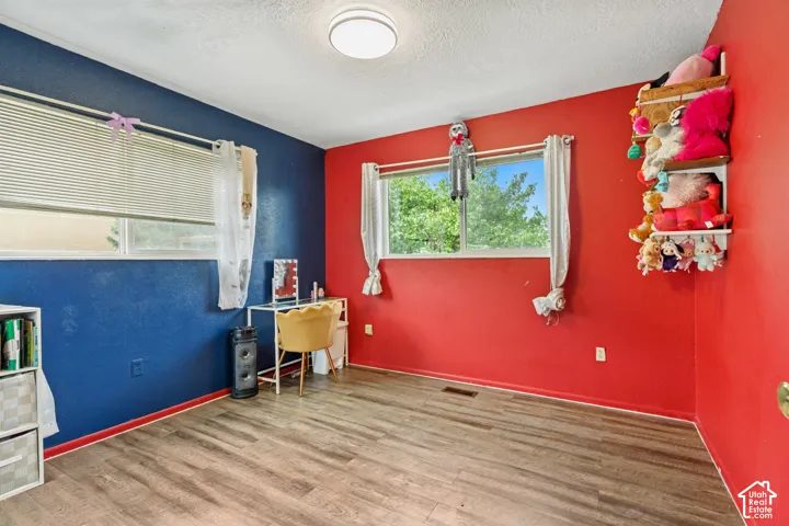Bedroom featuring wood-finish flooring, dual windows with horizontal blinds, and a flush-mount ceiling light fixture