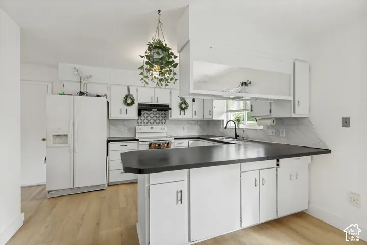 Kitchen featuring white cabinetry, solid surface countertops, patterned tile backsplash, wood-finish flooring, and a matte black faucet