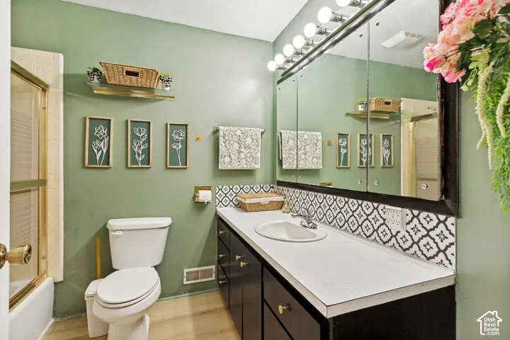 Bathroom featuring a vanity with dark cabinetry, solid-surface countertop, integrated basin, patterned tile backsplash, and a large multi-panel medicine cabinet with integrated lighting