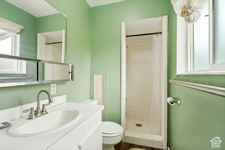 Bathroom featuring a white vanity cabinet with an integrated sink, a wide-frame wall mirror, a tiled walk-in shower, and a polished metal high-arc faucet