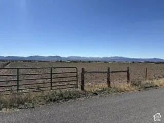 Expansive level acreage featuring a metal tubular gate and perimeter wood-post fencing with distant mountain scenery