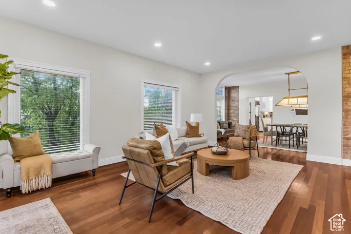 Living area featuring wood-finish flooring, recessed lighting, exposed brick pillar, and arched entryway