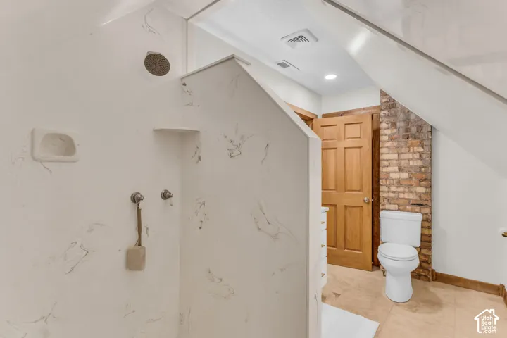 Shower enclosure featuring stone-pattern wall surrounds, integrated corner shelving, and a wall-mounted shower head, complemented by an exposed brick accent wall and tile flooring
