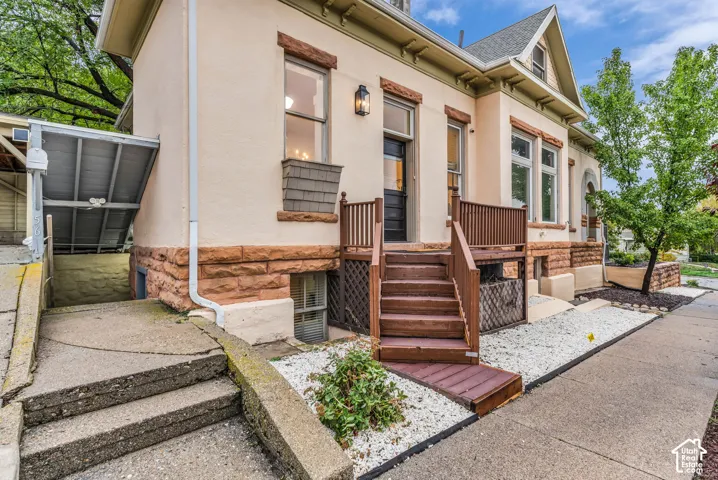 Historic exterior featuring stone foundation masonry, stucco siding, wood-toned porch stairs, gabled roofline, and custom window pediments