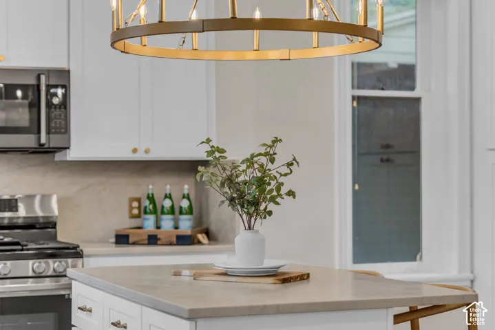 Circular metal chandelier with candelabra-style lighting, stone-surface kitchen island, white cabinetry, integrated microwave, and stone-surface backsplash