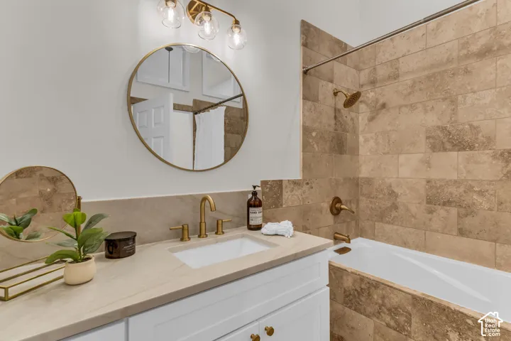 Bathroom featuring a white vanity with a neutral countertop, undermount sink, brass-finish hardware, round mirror, and tile-surround bathtub