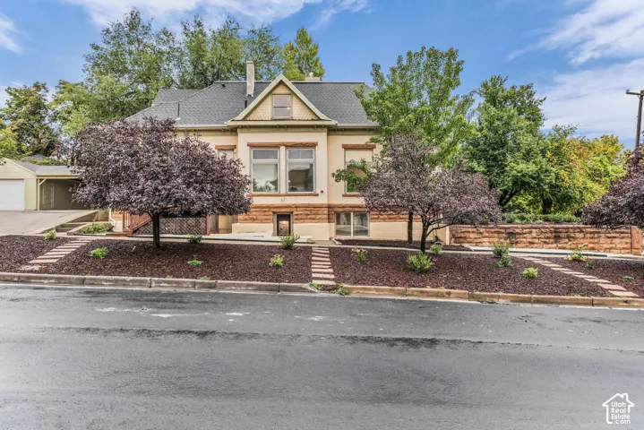 Exterior featuring stone masonry foundation, steep-pitched gable roof, multi-pane windows, and landscaped grounds with mature trees