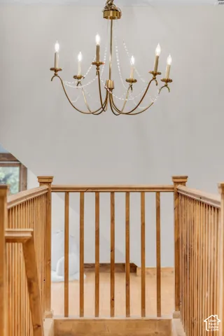Six-light candelabra chandelier with brass-finish hardware and integrated beaded detailing, complemented by natural wood-finish railings and balusters