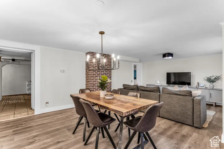 Open-concept living space featuring wood-finish flooring, a floor-to-ceiling exposed brick chimney, and a multi-arm metal chandelier