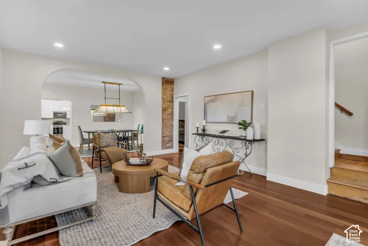 Living area featuring wood-finish flooring, recessed lighting, a decorative arched opening, and an exposed brick accent pillar