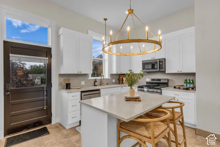Kitchen featuring shaker-style cabinetry, quartz countertops, a central island, a gold-tone chandelier, and stone-finish tile flooring