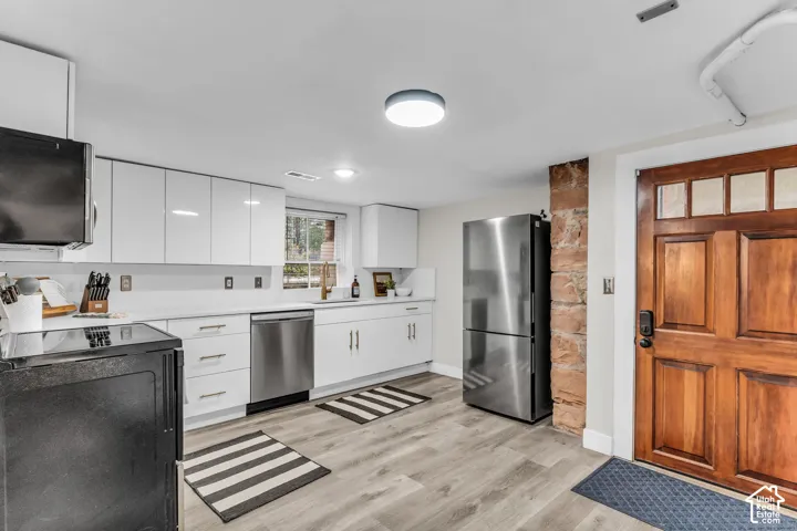 Kitchen featuring white flat-panel cabinetry, wood-finish flooring, stainless steel appliances, exposed stone accent wall, and a six-panel wood door with glass insets