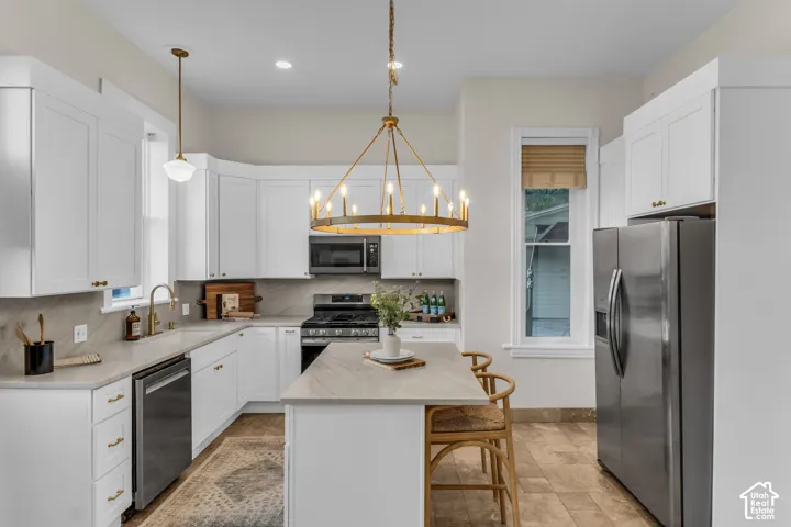 Kitchen featuring white shaker-style cabinetry, stone-surface countertops, a center island, stainless steel appliances, and a decorative metal chandelier