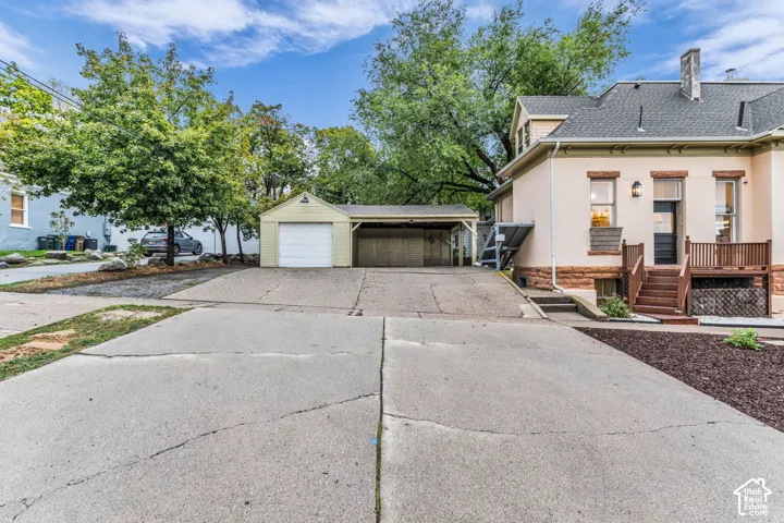 Exterior featuring a detached garage with an attached carport, expansive paved driveway, and stone foundation masonry
