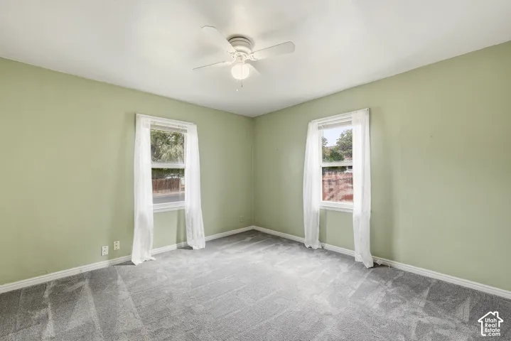 Interior room featuring neutral wall-to-wall carpeting, two double-hung windows, and a ceiling-mounted fan with integrated lighting