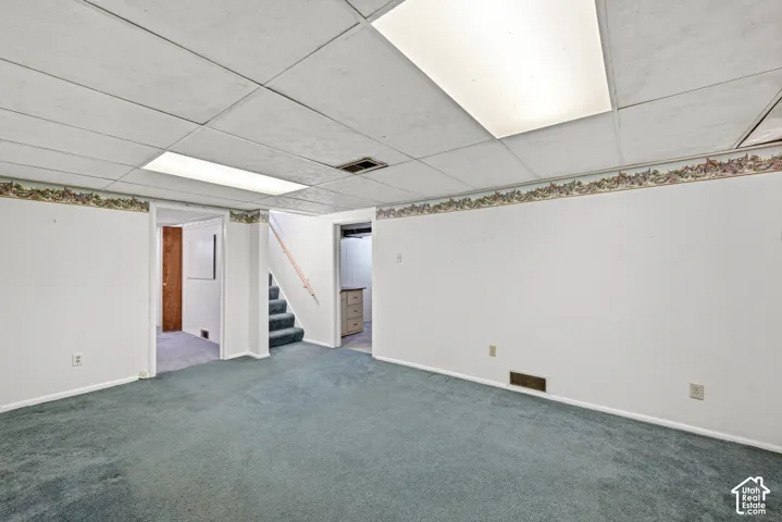 Open-concept interior space featuring wall-to-wall carpeting, a drop-in ceiling with integrated rectangular lighting, and painted walls with decorative border trim