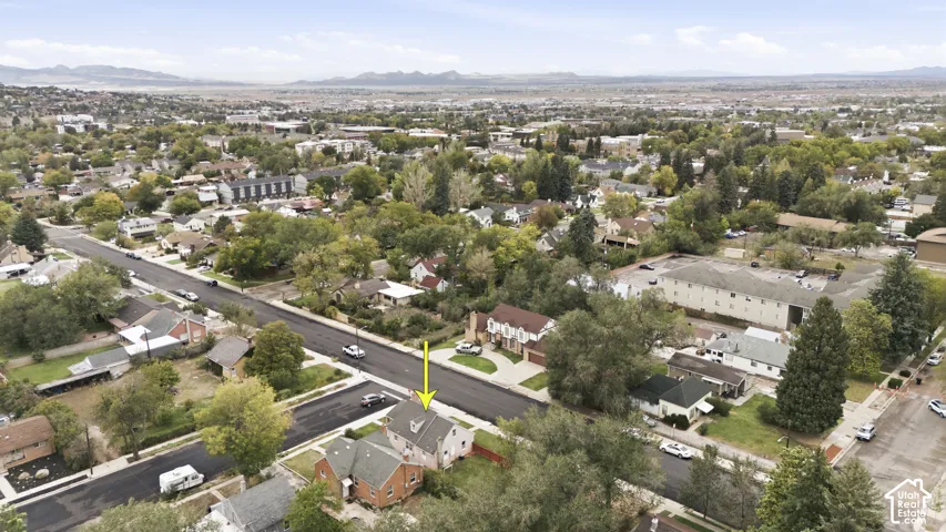 Aerial perspective of a detached residence featuring a pitched roof, brick exterior, corner lot positioning, and expansive surrounding mountain topography