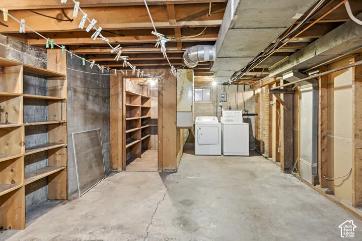 Unfinished utility area featuring concrete flooring, exposed wood joist ceiling, built-in wooden shelving units, and dedicated laundry hookups