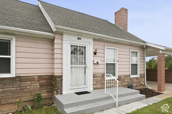 Exterior facade featuring horizontal siding, decorative stone masonry, a covered porch with a support pillar, and a brick chimney