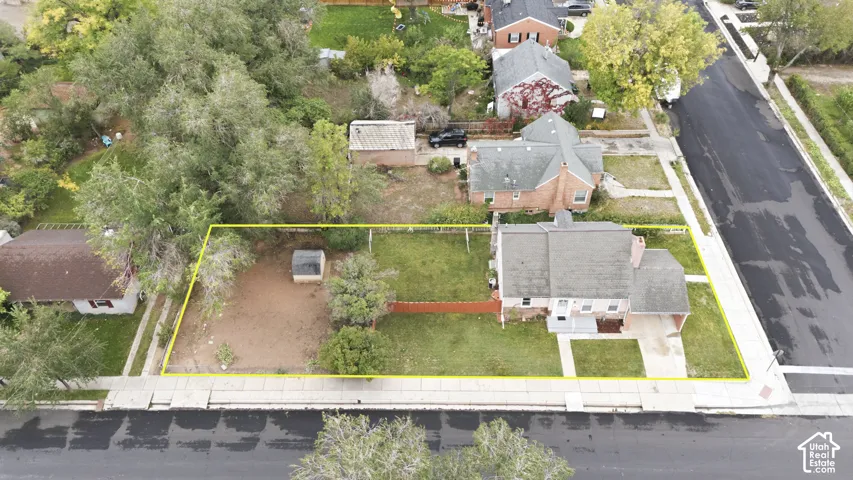 Aerial perspective of a corner lot property featuring a single-story brick home, a detached storage structure, mature trees, and perimeter fencing
