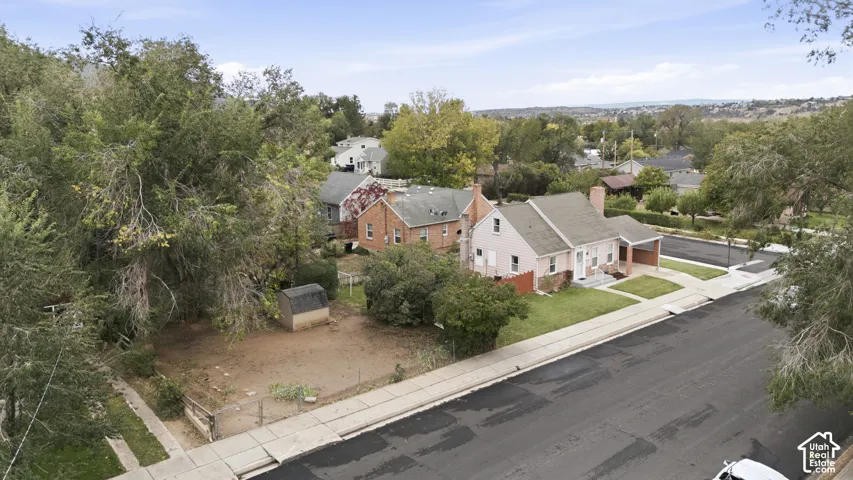 Exterior view of a residence featuring a pitched roofline, brick chimney, attached carport, and a detached storage shed on a lot with mature trees