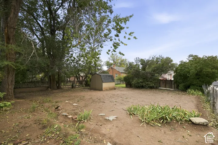 Expansive backyard featuring mature trees, a detached storage structure with a shingled roof, and perimeter fencing