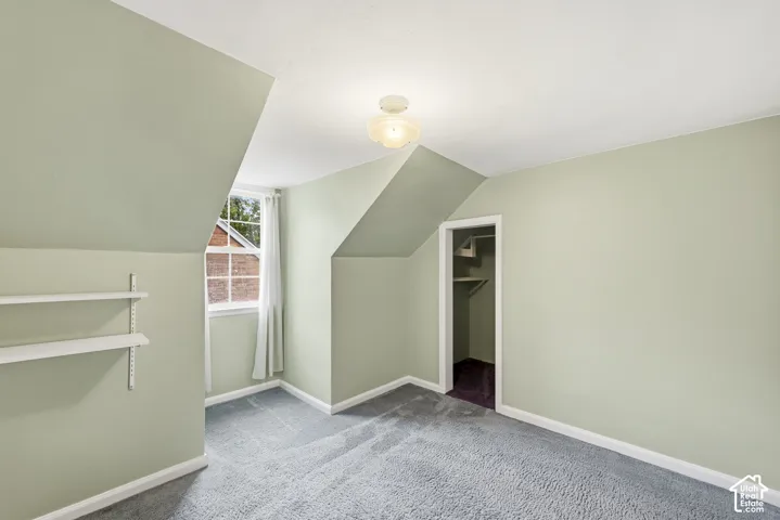 Room with wall-to-wall carpeting, vaulted ceiling lines, built-in shelving, a closet with integrated storage, and a multi-pane window
