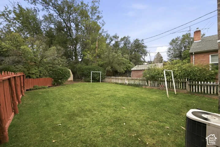 Backyard featuring a manicured lawn, perimeter wood fencing, mature trees, and brick exterior construction