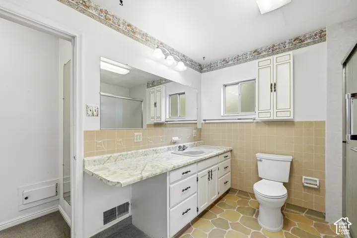 Bathroom featuring a vanity with stone-finish countertop, white cabinetry with matching wall-mounted storage, tile backsplash, and multi-tonal hexagonal floor tile