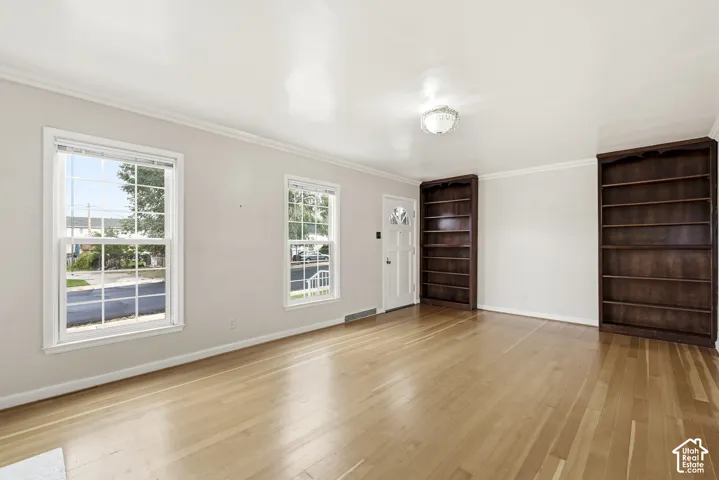 Neutral-toned interior featuring wood-finish flooring, two floor-to-ceiling built-in dark wood bookcases, double-hung windows, and crown molding