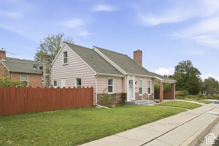 Exterior featuring horizontal siding, brick masonry base, attached carport, red wood-style fence, and brick chimney