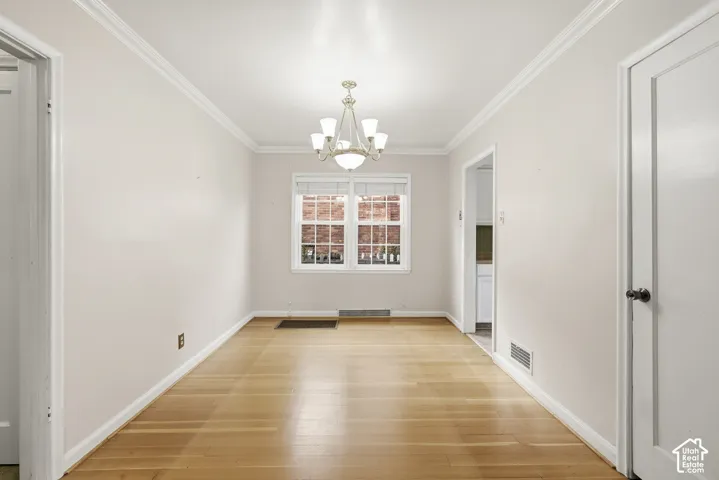 Neutral-toned interior space featuring wood-finish flooring, crown molding, a five-light chandelier, and a multi-pane window